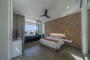 A modern bedroom with a large bed, a ceiling fan, a brick wall, and a view through a large window.