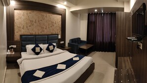 Habitación de hotel moderna con una cama grande, un área de descanso pequeña, un escritorio y un televisor.