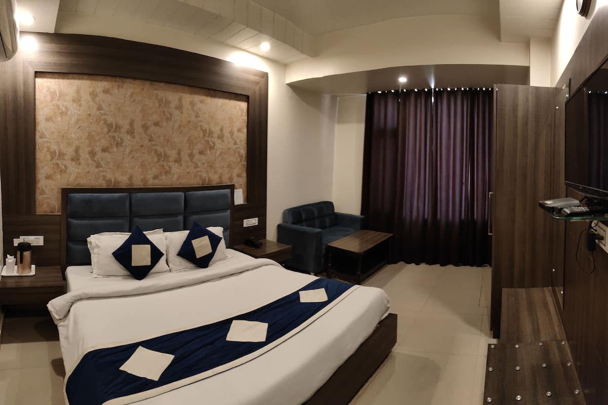 Habitación de hotel moderna con una cama grande, un área de descanso pequeña, un escritorio y un televisor.