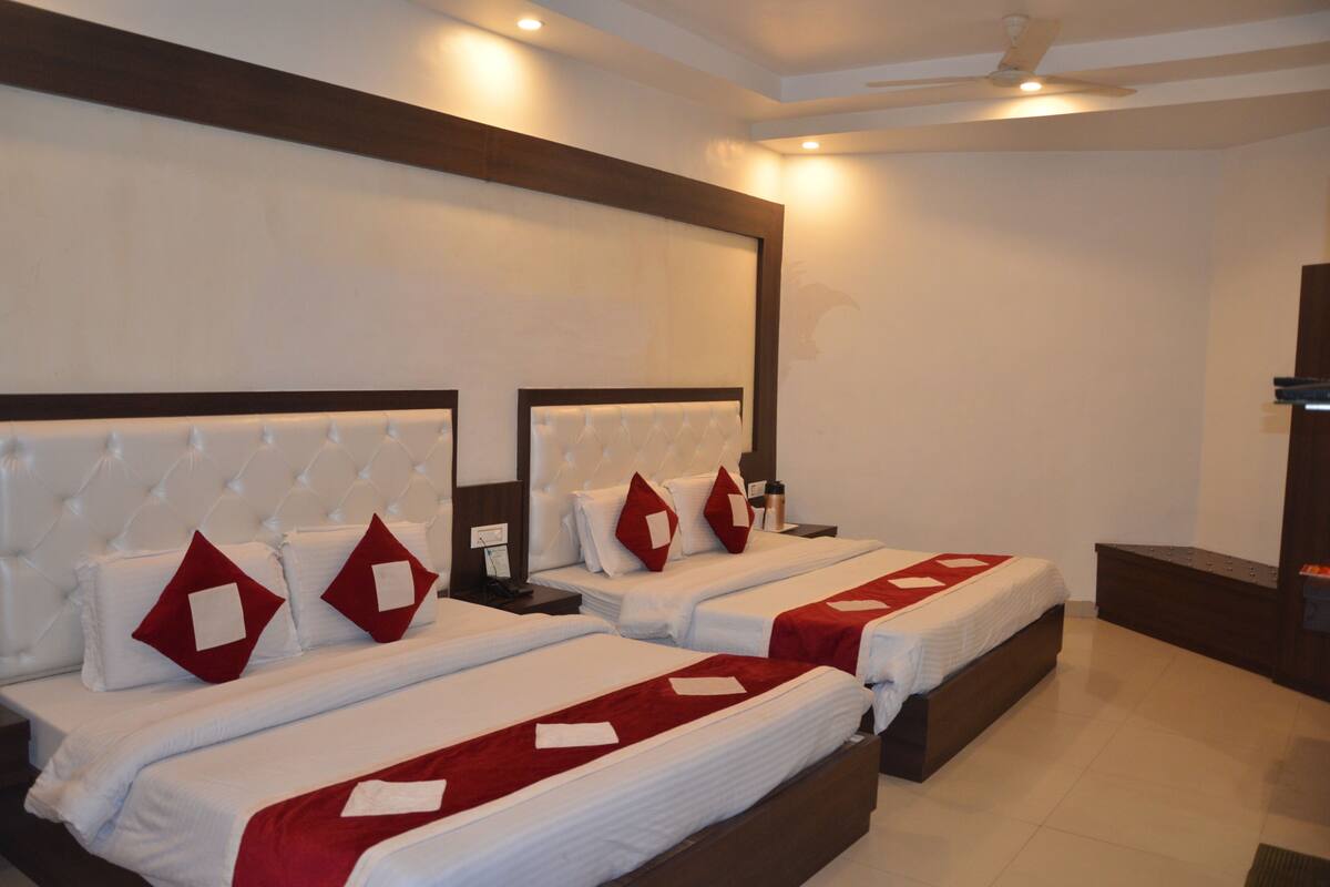 Habitación de hotel con dos camas, cada una con cabecera y almohadas. Hay una mesita de noche con una lámpara y una botella de agua.