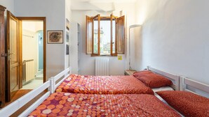 A bedroom with two beds, a window with an open shutter, a radiator, and a door leading to another room. - Appartamento San Gallo (Florence)