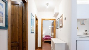 A hallway with a tiled floor, wooden doors, and white walls. There is a bed with a pink polka dot blanket in the background. - Appartamento San Gallo (Florence)