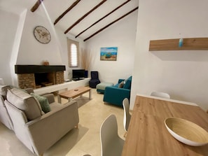 Een woonkamer met een stenen openhaard, een televisie, een bank, een eettafel en een schilderij aan de muur.