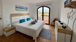 Un dormitorio con cama, mesita de noche, escritorio, silla, ventana y vistas al exterior.