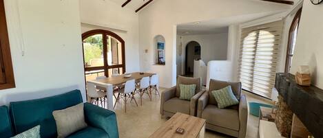 A spacious living area with a wooden dining table, a sofa, and a coffee table. There is a ceiling fan and a fireplace.