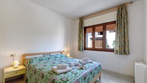 A bedroom with a bed, bedside tables, a window with curtains, and a radiator. - Delfino 3 Few Minutes From Sea (Loiri Porto San Paolo)