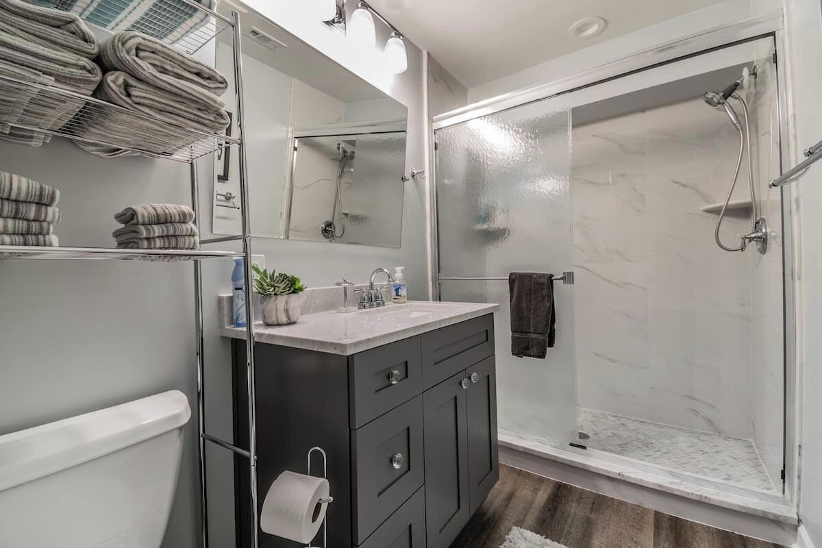 A modern bathroom with a glass shower enclosure, a vanity with a marble countertop, and a towel rack with folded towels.