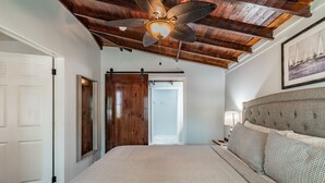 A bedroom with a large bed, wooden ceiling beams, a ceiling fan, and a framed picture on the wall. - Downtown Dunedin B&B  Casa w/ Heated Pool (Dunedin)
