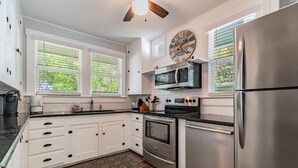 A modern kitchen with white cabinetry, stainless steel appliances, and a decorative clock. - Downtown Dunedin B&B  Casa w/ Heated Pool (Dunedin)