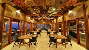 Un restaurant avec des tables et des chaises en bois, un plafond décoré de motifs et de grandes fenêtres.