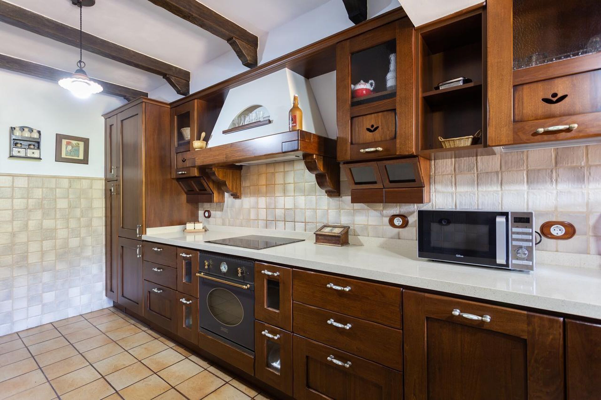 Een keuken met houten kastjes, een ingebouwde oven, een magnetron en een betegelde spatwand.