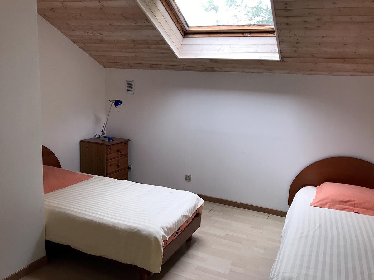 A bedroom with two beds, a wooden dresser, a desk with a lamp, and a skylight.