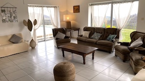 Un salon spacieux comprenant un canapé, des fauteuils, une table basse et une grande fenêtre donnant sur l’extérieur.