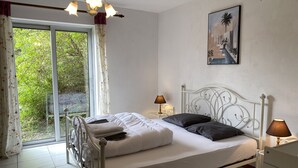 Une chambre à coucher avec un lit, deux lampes de chevet, une fenêtre avec des rideaux, un lustre et un tableau au mur.