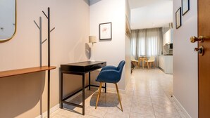 A modern hotel room with a desk, chair, and a view of the kitchen and dining area.