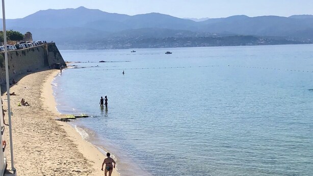 Una playa con arena, agua tranquila y montañas al fondo.