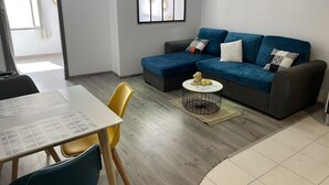 Un salón moderno con un sofá azul, una mesa de comedor con sillas y un reloj en la pared.