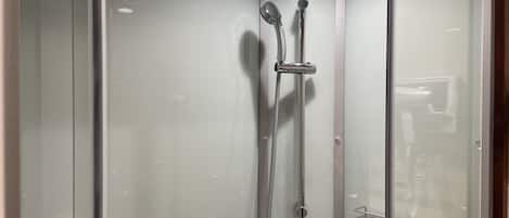 A glass-enclosed shower stall with a handheld showerhead, a wall-mounted faucet, and a handheld showerhead.