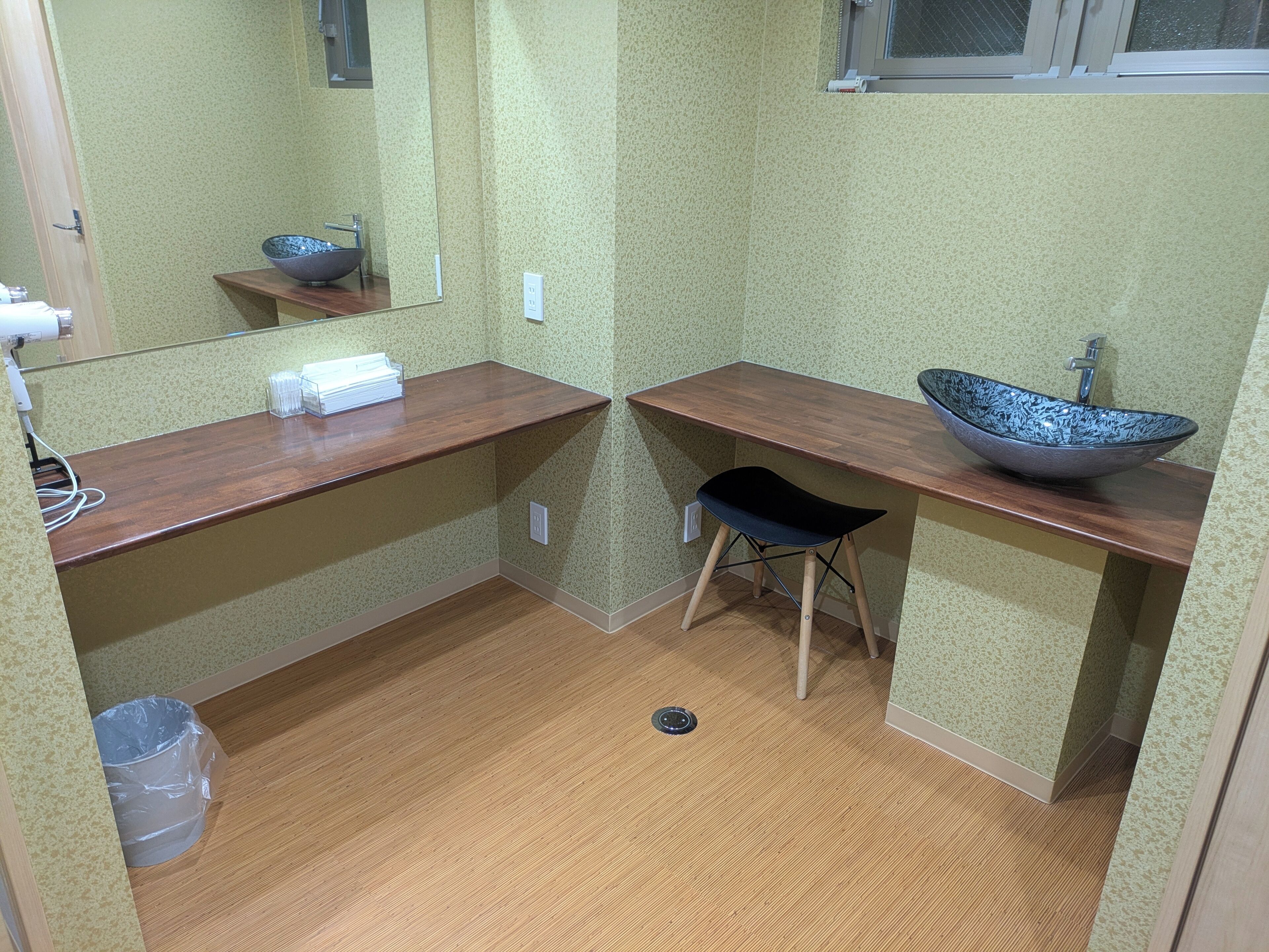 A small bathroom with a wooden vanity, a black stool, a large mirror, and a vessel sink.