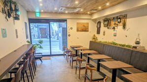 Un café con largas mesas y sillas de madera, un rincón con bancos y obras de arte en las paredes.