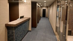 Zona de recepción de un hotel, con mostrador, pared estampada en azul y suelo alfombrado.