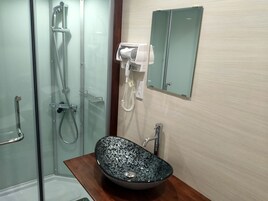 Un baño con ducha de vidrio, lavamanos con un recipiente decorativo, secador de pelo y espejo.