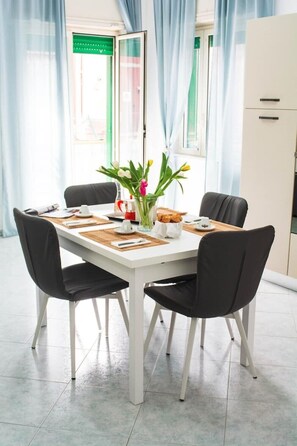 Un comedor con una mesa blanca, sillas negras y un jarrón de flores.