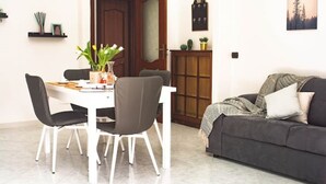 Ein Essbereich mit einem weißen Tisch, vier Stühlen, einem dunklen Sofa und einem Schrank mit Spiegel und Uhr.