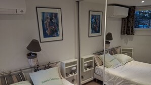 Une chambre d’hôtel avec deux lits, un miroir, une table de chevet avec une lampe, un tableau encadré et une fenêtre avec des rideaux.