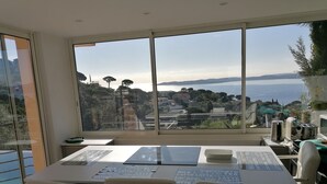 Un bureau moderne doté d’une grande fenêtre donnant sur un paysage côtier magnifique, avec des bâtiments et de la végétation.