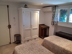 A bedroom with a wardrobe, a bedside table, a bed with patterned bedding, a window with curtains, and an air conditioning unit. - Sainte-Maxime Heated Pool Stunning view of Saint-Tropez - 2 suites (Sainte-Maxime)