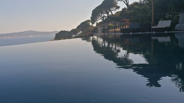Une piscine à débordement offrant une vue sur la mer et les collines lointaines.