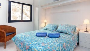 A bedroom with a bed, two bedside lamps, a chair, and a window with a view of bare trees. - Nautic Golf Playa C II by Interhome (Pals)