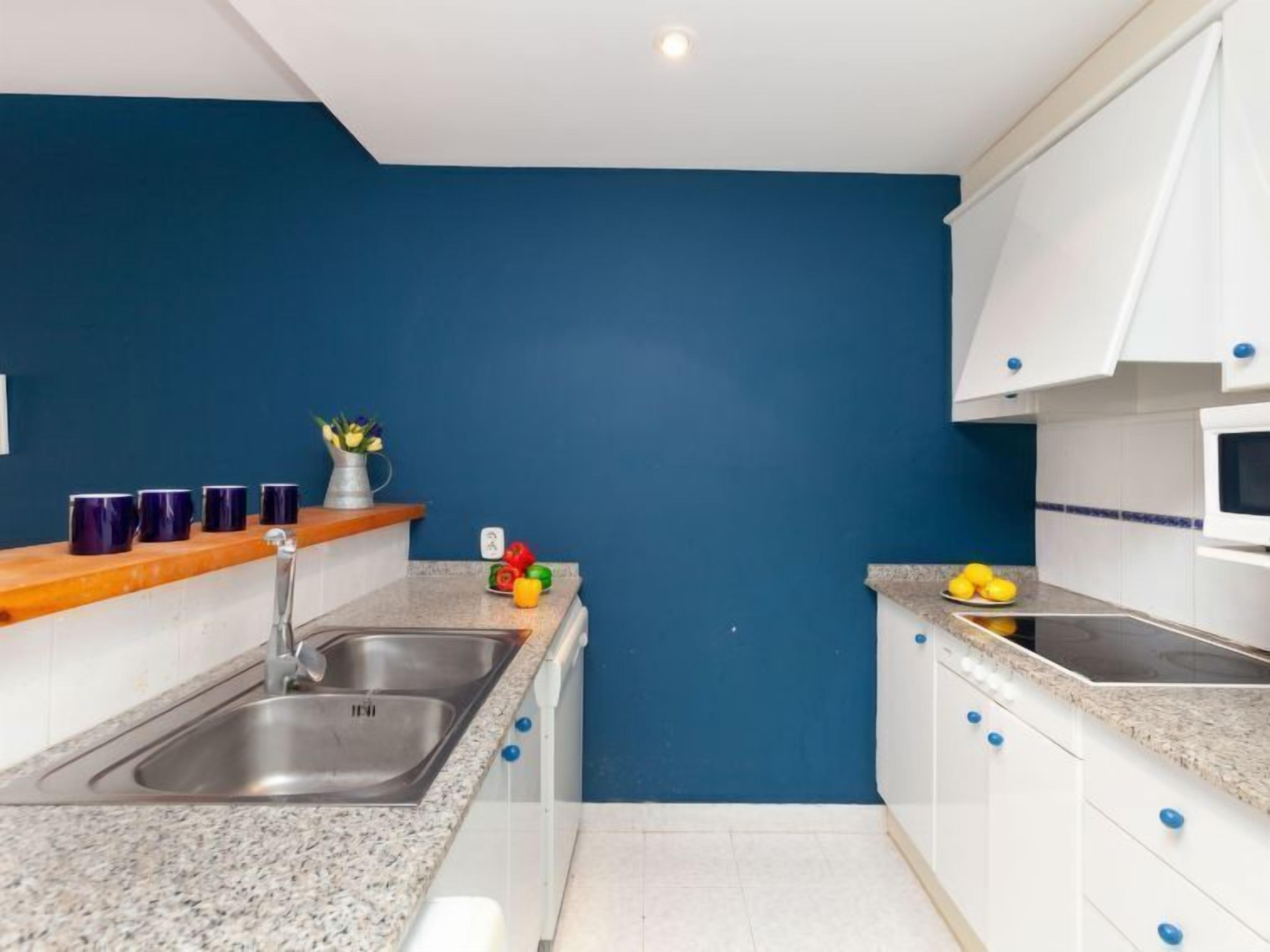 A compact kitchen with a blue accent wall, stainless steel sink, and white cabinets.