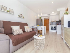 Ein modernes Wohnzimmer mit einer braunen Couch, einem runden Couchtisch und einer Küche im Hintergrund.