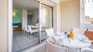 Ein Essbereich mit Tisch für zwei Personen, einer Couch und einer Glastür zum Balkon.