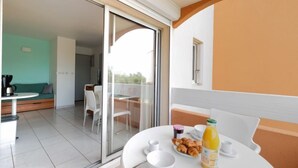 Ein Balkon mit Esstisch, gedeckt für ein Frühstück, darunter Croissants und Saft, sowie eine Couch und im Hintergrund eine Kaffeemaschine.