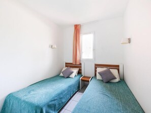 A room with two single beds, a window with curtains, and a small bedside table. - Primavera by Interhome (Cap d'Agde)
