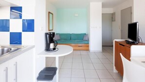 Ein kompaktes Hotelzimmer mit Küchenzeile, einer Couch, einem Fernseher und einer Kaffeemaschine.