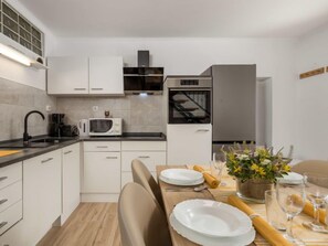 Cozinha moderna com armários brancos, bancada preta e área de jantar com mesa de madeira posta para dois.