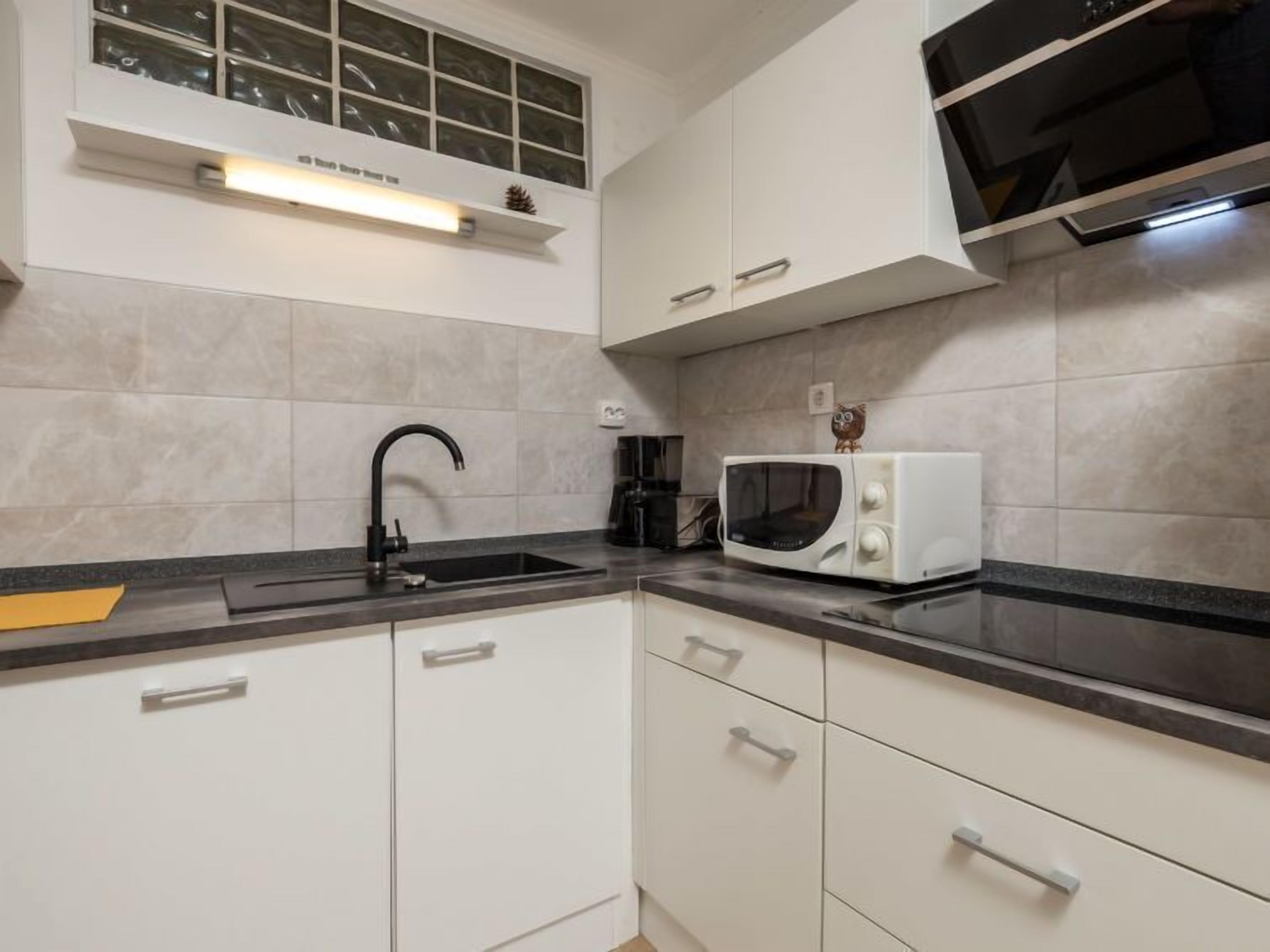 Moderni keittiö, jossa on valkoiset kaapit, musta pesuallas, mikroaaltouuni ja ikkuna pesualtaan yläpuolella.