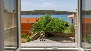 A view from a window overlooking a courtyard with a stone wall, a small pool, and a view of the sea and hills in the distance.