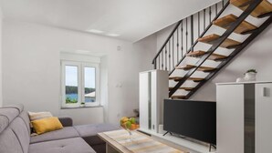 A modern living room with a grey sofa, a flat-screen TV, a wooden staircase, and a window with a view.
