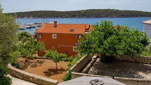 A coastal property with a red-roofed building, a garden with trees, and a view of the sea and boats.