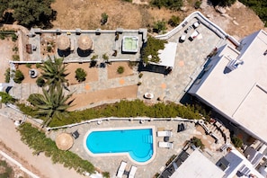 An aerial view of a resort with a swimming pool, outdoor seating areas, and a hot tub.