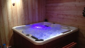Una cabaña de madera con un jacuzzi lleno de agua e iluminado con luces azules.