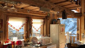Una cocina rústica con vigas de madera, un refrigerador blanco, un microondas y vistas a montañas nevadas a través de amplios ventanales.