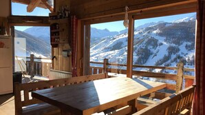 Comedor de madera con una mesa y bancos, ventanas amplias con vistas a las montañas y techo de madera.