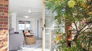 An open-plan living area with a sofa, wicker furniture, and a view through a glass door to a balcony.