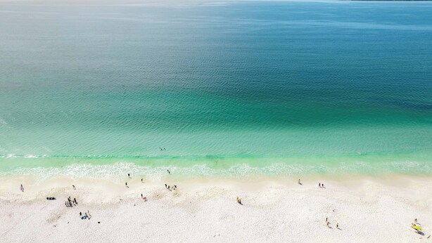 A beach with clear turquoise water, sandy shore, and distant land.